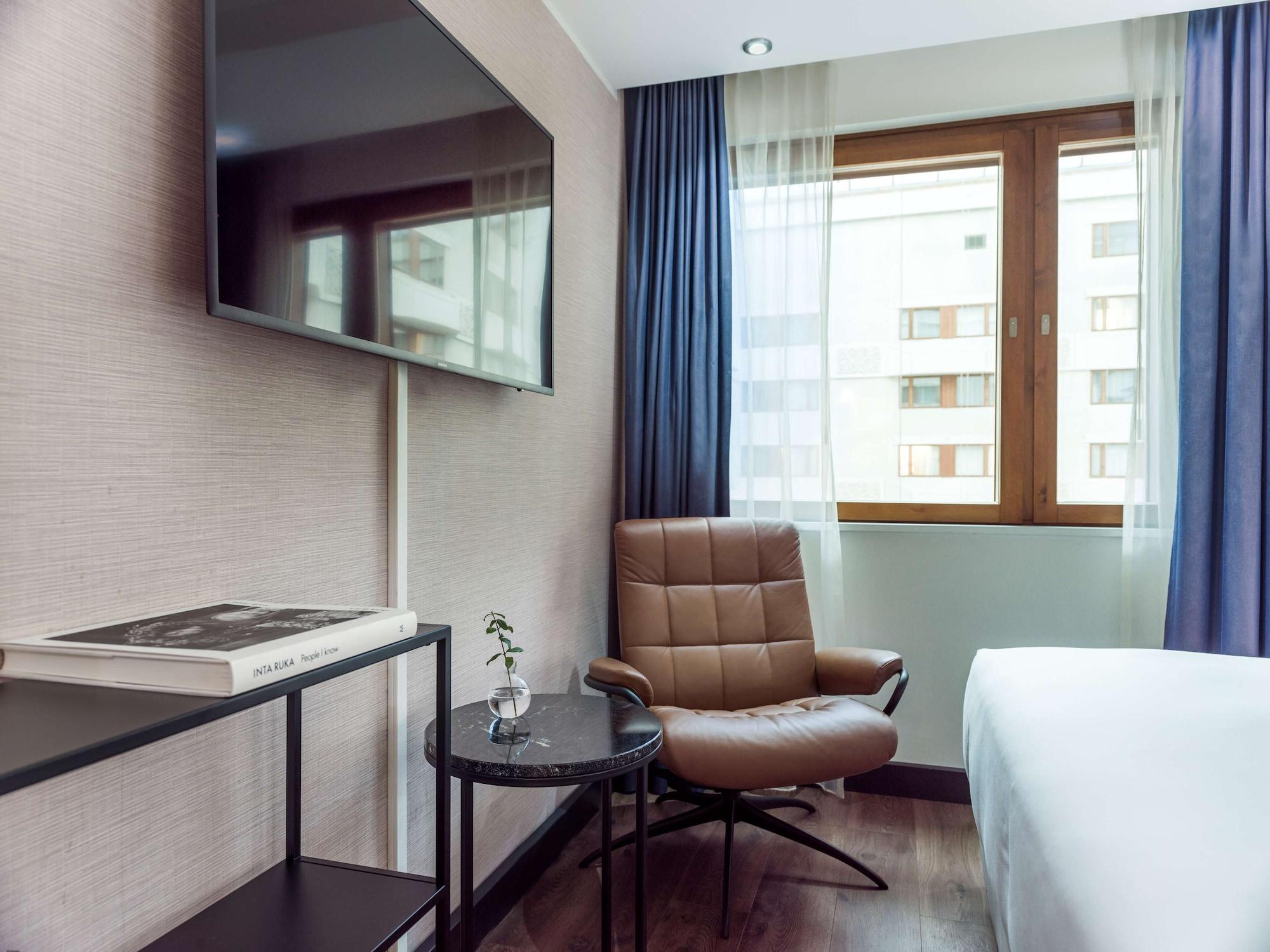 Radisson Blu Royal Viking Hotel, Stockholm Exterior foto The photo shows a modern hotel room featuring a comfortable arrangement. There is a large flat-screen TV mounted on the wall. Below the TV, a sleek, minimalistic table holds a book and a small decorative plant. Next to the table is a stylish brown ch