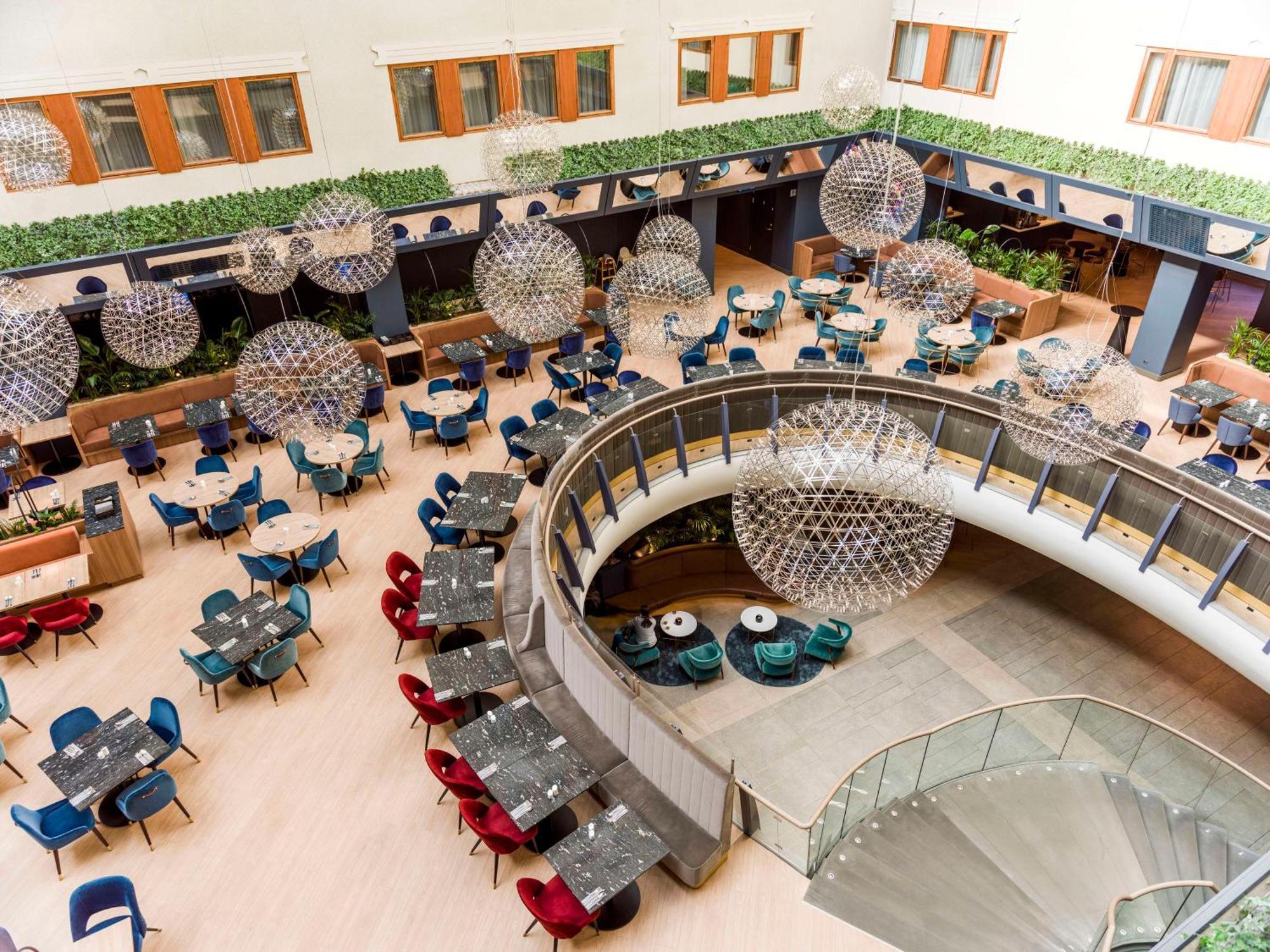 Radisson Blu Royal Viking Hotel, Stockholm Exterior foto The photo shows a spacious and stylish dining area in a modern restaurant or hotel lobby. It features a variety of round tables arranged in a curved layout, surrounded by colorful chairs in shades of blue, red, and gray. Large, spherical light fixtur